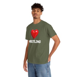 Op de afbeelding: Olijfgroen t-shirt met een rood hart en het woord "WRESTLING" in het wit. Het t-shirt is gemaakt van zacht materiaal en heeft korte mouwen. Een casual top voor worstelfans.