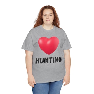 Op de afbeelding: Grijs t-shirt met een groot rood hart en het woord "HUNTING" in zwarte, vette letters. Het shirt is gemaakt van een zacht materiaal en is geschikt voor casual wear.