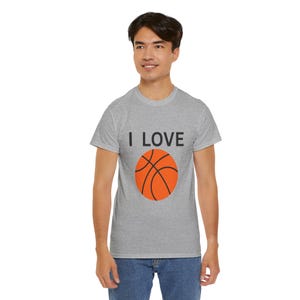 Op de afbeelding: Een grijs t-shirt met de tekst "I LOVE" boven een oranje basketbalafbeelding. Het shirt is gemaakt van een zacht materiaal en is geschikt voor vrijetijdskleding. Het ontwerp is eenvoudig en gedurfd, perfect voor basketbalfans.