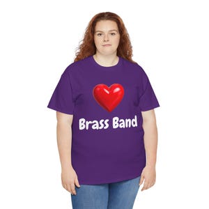 Op de afbeelding: Een paars T-shirt met een rode hartafbeelding en de witte tekst "Brass Band". Het shirt is gemaakt van een zacht materiaal en is geschikt voor vrijetijdskleding. Het ontwerp is eenvoudig en opvallend, ideaal voor muziekliefhebbers.