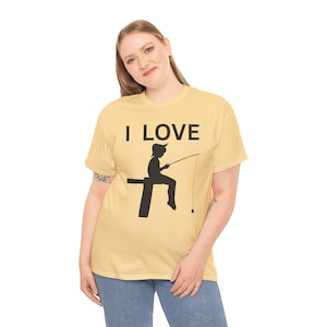 Op de afbeelding: Lichtgeel t-shirt met de tekst "I LOVE" boven een zwart silhouet van een visser. De persoon zit op een pier en houdt een hengel vast met een dobber in het water.