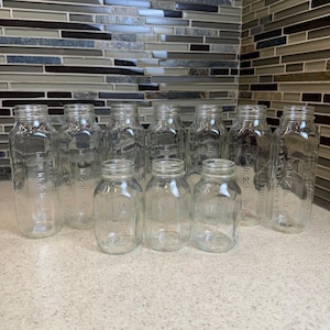 Puede incluir: Una colección de diez botellas de vidrio transparente dispuestas en dos filas. Las botellas más altas en la parte posterior y las más cortas en el frente presentan el texto en relieve EVENFLO en el lateral. Cada botella tiene un cuello estrecho.