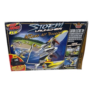 May include: A boxed Air Hogs Storm Launcher RC toy. The box features a white, yellow, and black hydrofoil design with propellers. Text on the box reads "Insane All Terrain!" and "Ready to Run". The box also shows images of the toy in action.