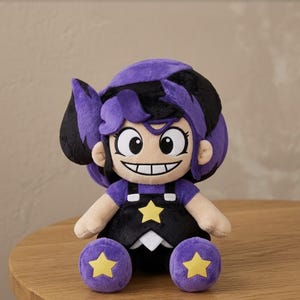 May include: A plush doll featuring a character with purple and black hair, large white eyes, and a wide grin. The doll wears a black overall dress with a yellow star on the chest and purple shoes, each decorated with a yellow star on the front.
