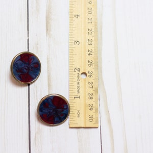 May include: A pair of round, gold-toned earrings with a blue and red marbled design.
