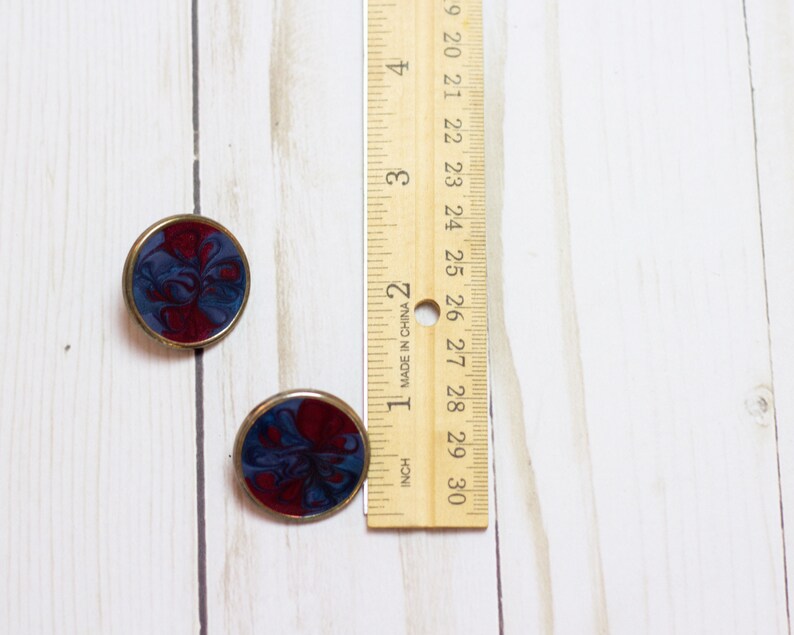 May include: A pair of round, gold-toned earrings with a blue and red marbled design.