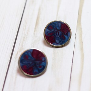 May include: Two round, silver-toned earrings with a blue and burgundy marbled design.