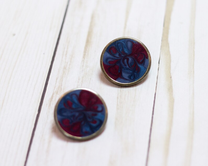 May include: Two round, silver-toned earrings with a blue and burgundy marbled design.
