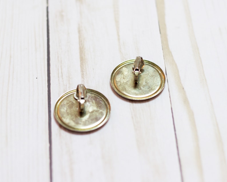 May include: A pair of gold-toned clip-on earrings with round, smooth, metal fronts.
