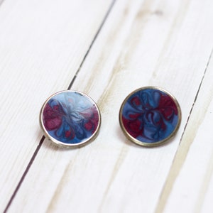 May include: A pair of round earrings with a silver metal setting and a blue and red marbled design.