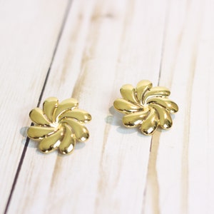 May include: A pair of gold-tone earrings with a flower design. The earrings are made of metal and have a shiny finish.