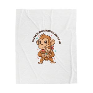 May include: A white blanket featuring a cartoon monkey holding a smaller monkey plush. The monkey wears a red bandana and the text "HOLD ON TO WHAT REMINDS YOU WHO YOU ARE" is arched above the monkey.