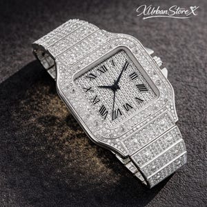 K&ouml;nnte beinhalten: Silberfarbene Armbanduhr mit quadratischem Zifferblatt und Armband, vollst&auml;ndig mit glitzernden Kristallen besetzt. Das Zifferblatt hat schwarze Zeiger und r&ouml;mische Ziffern. Der Text "Xurban Store X" ist oben rechts zu sehen.