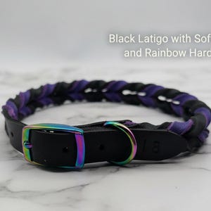 May include: A braided collar made of black and soft purple leather featuring iridescent rainbow-colored metal hardware, including a buckle and a D-ring. The text Black Latigo with Soft Purple and Rainbow Hardware is visible above the collar.