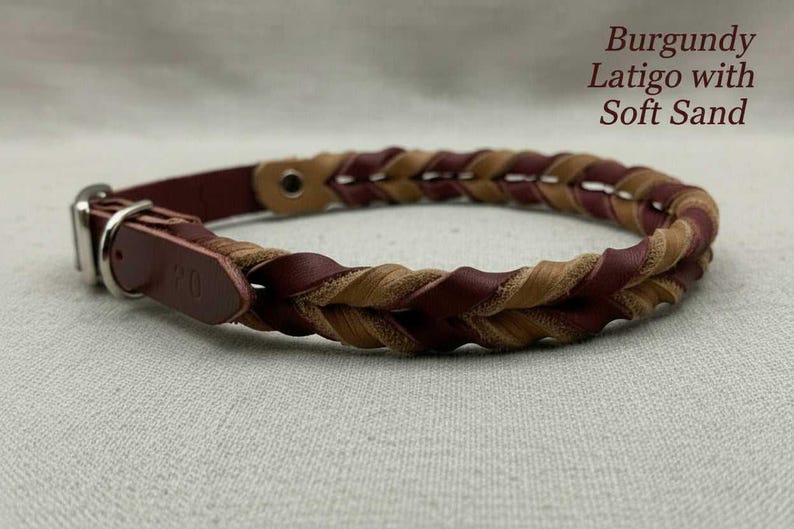 May include: A braided leather collar featuring alternating burgundy and soft sand colored strands. The collar includes a silver-toned metal buckle and a leather strap end. Text on the image reads: Burgundy Latigo with Soft Sand.
