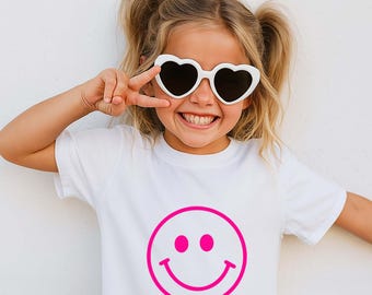 May include: A white t-shirt with a large pink smiley face graphic. The person is wearing white heart-shaped sunglasses. The person is smiling and giving a peace sign.