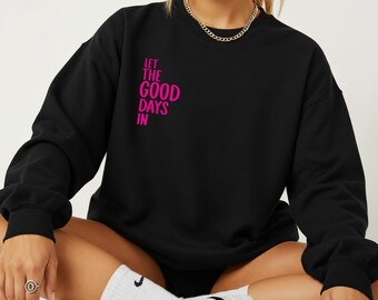 May include: Black sweatshirt with the text "LET THE GOOD DAYS IN" in bright pink. The sweatshirt has a crew neck and long sleeves. The text is printed on the upper left chest area.