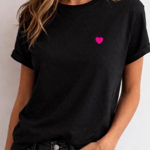 Może przedstawiać: Czarny t-shirt z małym, jasnor&oacute;żowym sercem wyhaftowanym na lewej piersi. Kr&oacute;tkie rękawy są podwinięte. Koszulka wykonana jest z miękkiego materiału.