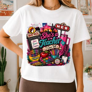 May include: A white t-shirt featuring a colorful graphic print with the text She's a Teacher I Can Tell, Buc-ee's and H-E-B logos, a Texas silhouette, a cactus, a notebook, crayons, a red apple, a paint set, scissors, and a pink tumbler.