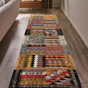 Peut inclure: Un tapis rectangulaire multicolore avec un motif patchwork. Le tapis présente divers motifs géométriques et couleurs, notamment du rouge, du bleu, du jaune et du noir. Le tapis a une bordure à franges et est posé sur un parquet.