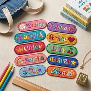 May include: Ten oval embroidered name patches in various colors, each featuring a unique icon like a flower, butterfly, crown, rainbow, tulip, bow, heart, cherry, star, or rabbit. The names Emma, Sophia, Olivia, Grace, Chloe, Lily, Amelia, Harper, Mia, and Ava are stitched in colorful thread.