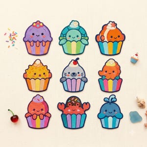 Op de afbeelding: Een verzameling van negen geborduurde patches in de vorm van cupcakes, elk met een ander zeedier zoals een schildpad, clownvis, kogelvis, zeehond, zeepaardje, octopus, krab en walvis, versierd met kleurrijke spikkels en kleine zeethema-accenten.