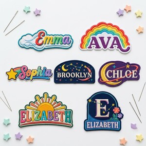 Op de afbeelding: Zeven geborduurde stoffen patches met diverse namen en ontwerpen, waaronder regenbogen, sterren, manen en sterrenbeelden. De namen Emma, Ava, Sophia, Brooklyn, Chloe en Elizabeth zijn met gekleurde draad op een witte achtergrond geborduurd.