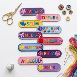 Puede incluir: Una colección de parches rectangulares bordados con nombres en varios colores como morado, rosa, amarillo y azul. Cada parche presenta un nombre único como CANER, DEFNE, SELIM, SERKAN, MELIS, TUĞBA, MERYEM, ESRA, AYŞEGÜL y ENES con iconos decorativos.