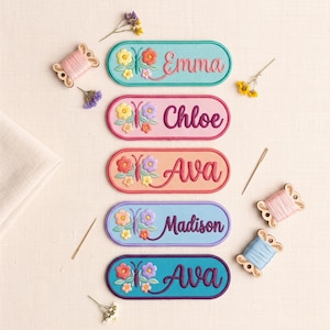 Op de afbeelding: Vijf ovale geborduurde patches met de namen Emma, Chloe, Ava, Madison en Ava. Elke patch toont een vlinder- en bloemmotief in diverse kleuren zoals turquoise, roze, perzik, lavendel en blauw, vergezeld door naainaalden en garen.