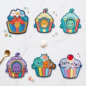 Puede incluir: Seis parches bordados con coloridos temas acuáticos. Los diseños incluyen un cangrejo en un cofre del tesoro, tres cupcakes con criaturas marinas y pajitas, un cupcake con una tortuga marina y un pez payaso, y otro con dos focas y una cereza.