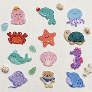 May include: A collection of embroidered fabric patches featuring various sea creatures including a pink octopus, teal dolphin, blue jellyfish, red crab, orange starfish, green turtle, teal whale, pink seashell, purple seahorse, purple stingray, and brown otter.
