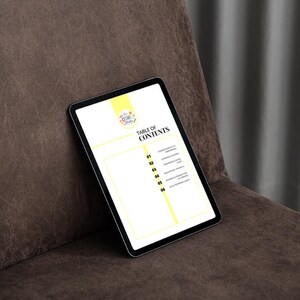 May include: A digital tablet displaying a "Table of Contents" page. The tablet has a black bezel and a bright yellow and white background. The tablet is resting on a brown leather surface.