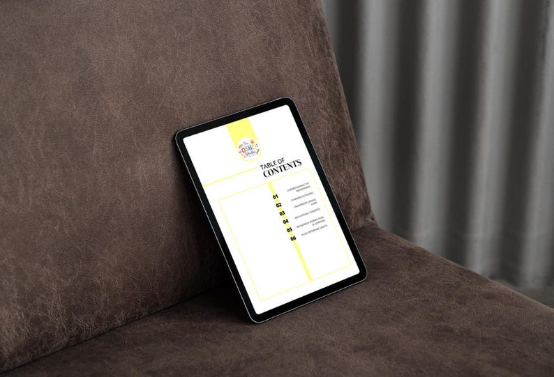 May include: A digital tablet displaying a "Table of Contents" page. The tablet has a black bezel and a bright yellow and white background. The tablet is resting on a brown leather surface.
