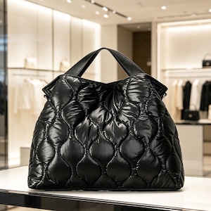 Peut inclure: Un sac fourre-tout noir matelassé avec une finition brillante. Le sac présente un motif en losange et deux poignées noires. Le sac est posé sur une surface blanche dans un cadre de magasin.