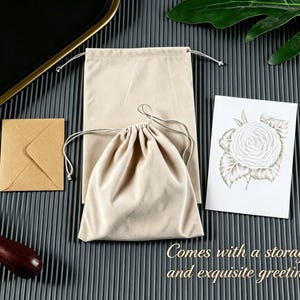 May include: A beige rectangular drawstring pouch, a smaller beige drawstring bag, a small square brown envelope, and a white rectangular greeting card featuring a detailed illustration of a white rose with green leaves and the text Comes with a storage bag and exquisite greeting card.