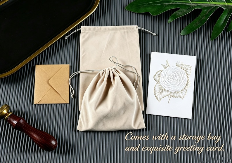 May include: A beige rectangular drawstring pouch, a smaller beige drawstring bag, a small square brown envelope, and a white rectangular greeting card featuring a detailed illustration of a white rose with green leaves and the text Comes with a storage bag and exquisite greeting card.