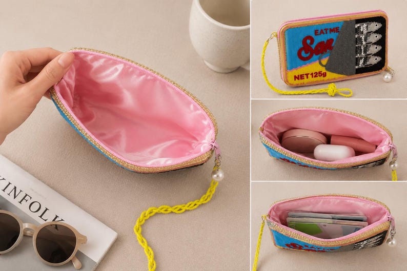 May include: A rectangular zippered pouch featuring a sardine tin graphic with the text EAT ME Sardines NET 125g. The exterior has a blue, yellow, and black design, while the interior is lined with pink satin. It includes a yellow braided wrist strap.