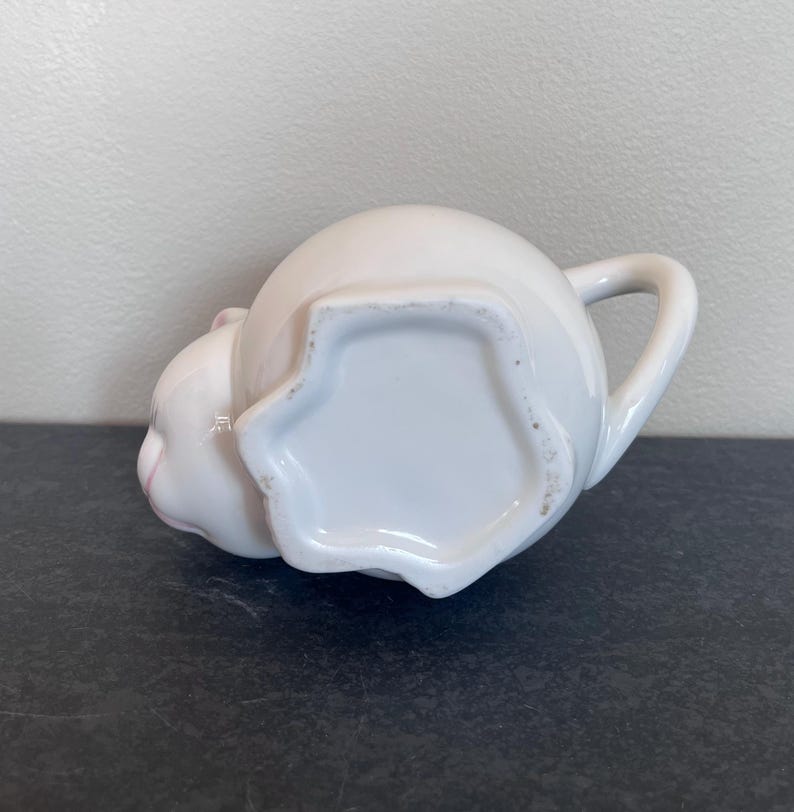 Może przedstawiać: Biały ceramiczny kubek z czarnym uchwytem i napisem "But First, Coffee" pogrubioną czcionką. Kubek jest ustawiony na rozmytym tle, sugerującym przytulne otoczenie.