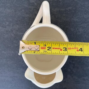 Może przedstawiać: Zestaw trzech ceramicznych kubk&oacute;w z nakrapianym, matowym wykończeniem. Kubki są w odcieniach kremu, jasnoszarym i ciemnoszarym. Każdy kubek ma prosty, minimalistyczny design i zaokrąglony uchwyt.