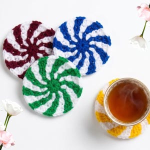 May include: Handmade crocheted coasters in red, blue, and green with white spiral stripes. A cup of tea rests on a yellow and white striped coaster. These coasters are a decorative addition to any home.