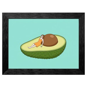 May include: A framed print featuring a cartoon illustration of a woman in an orange dress and sunglasses relaxing on a large avocado half. The avocado has a green, textured exterior and a brown pit, set against a light blue background.