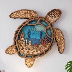 Peut inclure: Une grande décoration murale en bois multicouche en forme de tortue marine, présentant une scène sous-marine découpée au laser avec de l'eau bleue, du corail et un hippocampe. Deux autres décorations murales en bois assorties sont présentes.