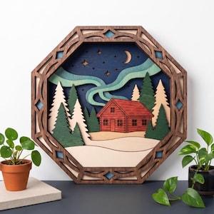 May include: An octagonal layered wooden wall art piece featuring a red cabin in a snowy forest under a dark blue night sky with a crescent moon, stars, and green aurora borealis. The frame has a dark brown finish with geometric cutouts.