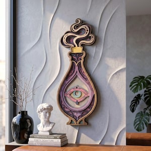 May include: A layered wooden wall art piece shaped like a potion bottle with a swirling smoke top. The design features a central eye motif in shades of purple, pink, and cream, with intricate cutouts and a gold-colored stopper detail.