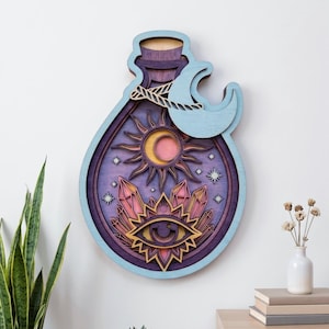 May include: A layered wooden wall art piece shaped like a potion bottle. The design features a central eye, crystals, a sun, and a crescent moon. The color palette includes shades of purple, light blue, yellow, and pink with a natural wood finish.