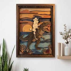 Op de afbeelding: Houten kunstwerk met meerdere lagen dat een poedelcowboy toont die op een Tyrannosaurus Rex rijdt. Het kunstwerk heeft een zonsondergangachtergrond met oceaan- en koraaldetails. Unieke, grillige wanddecoratie.