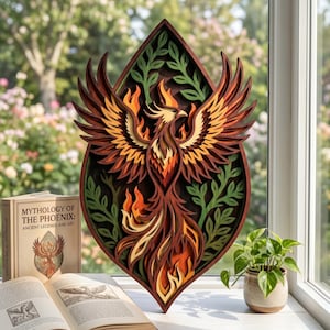 Op de afbeelding: Een meerlaagse houten sculptuur van een feniks in bruin-, oranje- en geeltinten, met groene bladeren. Het kunstwerk staat voor een raam, met een boek getiteld "Mythologie van de Feniks" in de buurt.