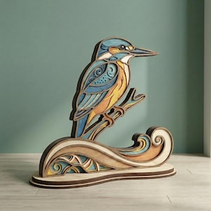 May include: A layered wooden sculpture of a kingfisher bird perched on a branch above a stylized wave. The bird features blue, yellow, and orange hues, while the base has a natural wood finish. The artwork is a decorative piece.