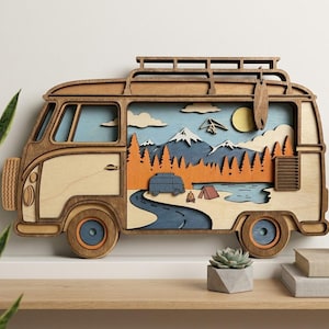 May include: A multi-layered wooden wall art piece shaped like a vintage camper van. The interior scene features a blue sky, a yellow sun, snow-capped mountains, orange pine trees, a winding road, a small campfire, and a tent near a blue lake.