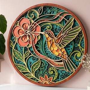 May include: A round, layered wooden wall art piece featuring a hummingbird and flower design. The hummingbird is depicted in shades of yellow, orange, and brown, with green wings. The flower is coral, and the background is teal and green.